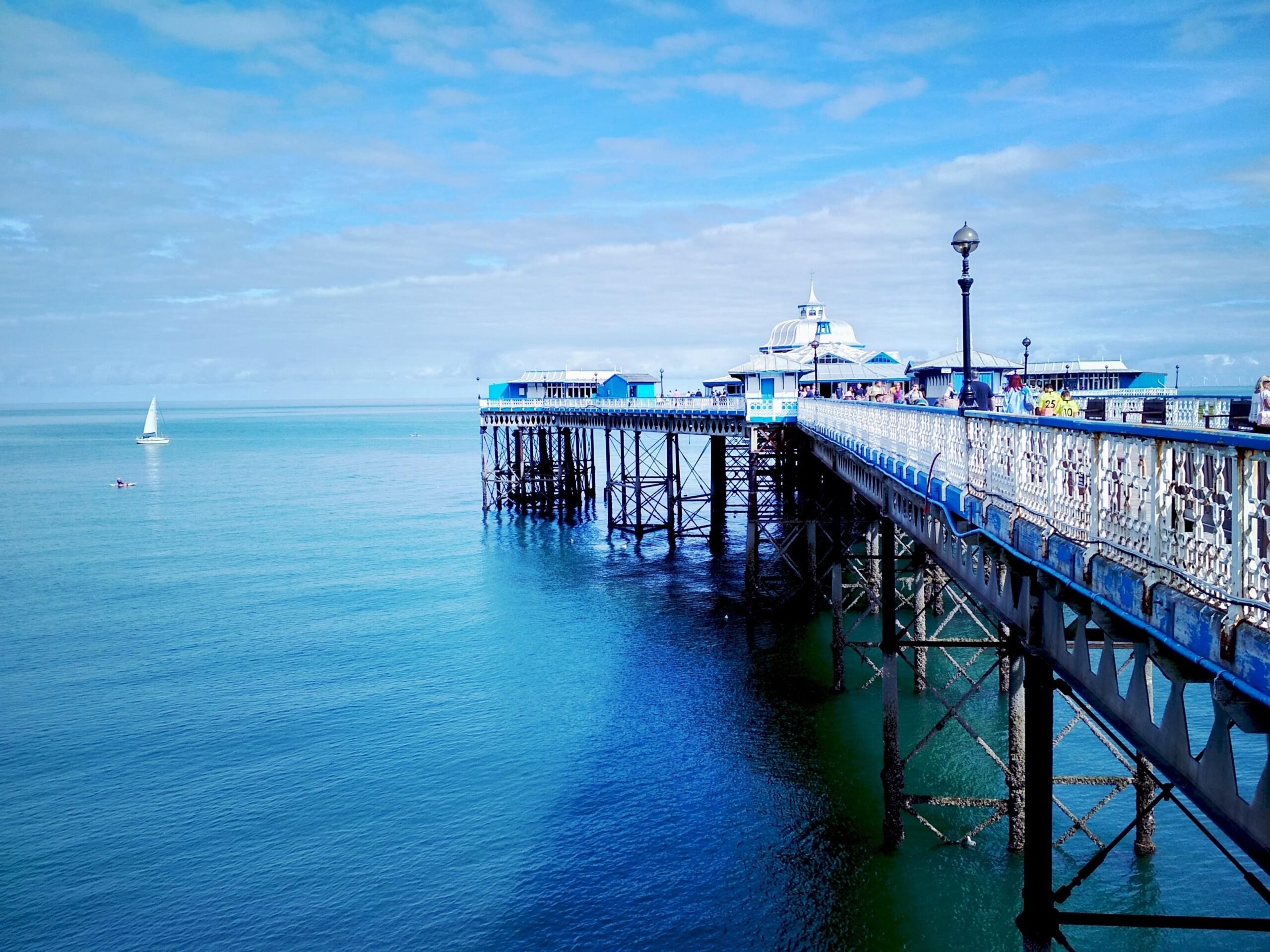 Pier in North Wales with blue sea blue sky and a small sail boat