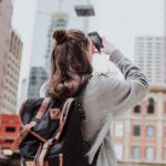 woman used her phone to take photos of the buildings in a city wearing a backpack and a grey sweatshirt