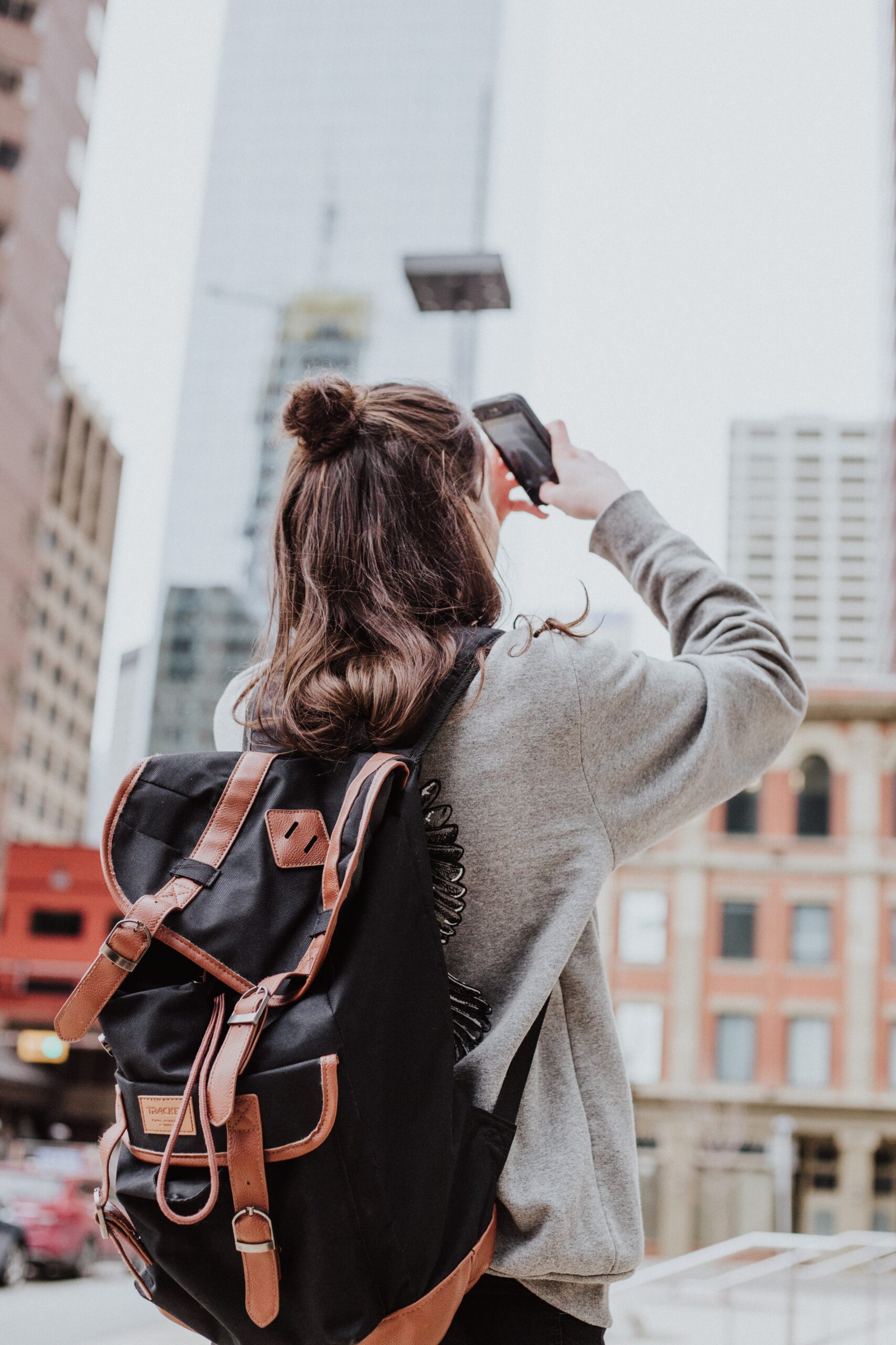 woman used her phone to take photos of the buildings in a city wearing a backpack and a grey sweatshirt