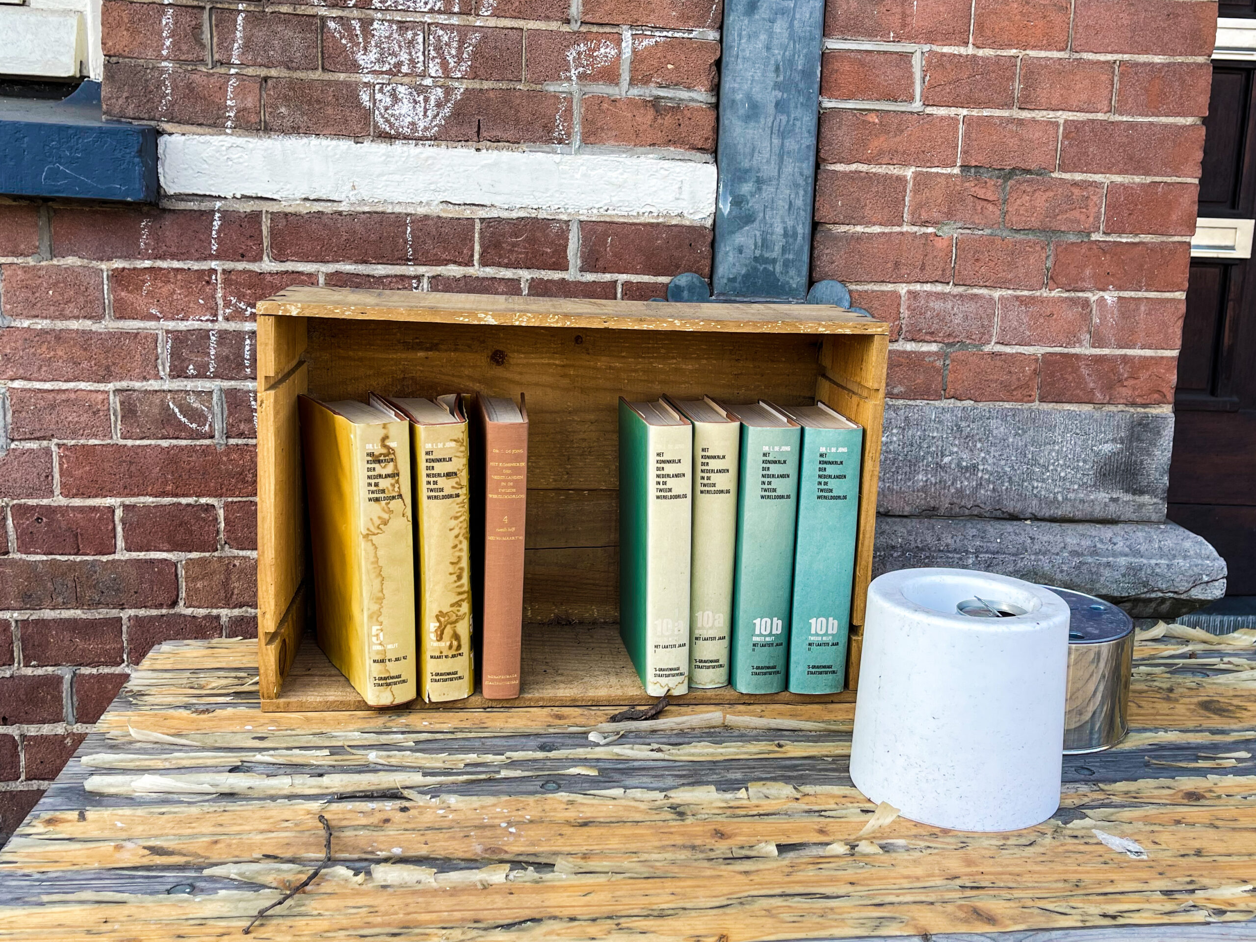 Colourful books in a small wooden box outside of a red brick house