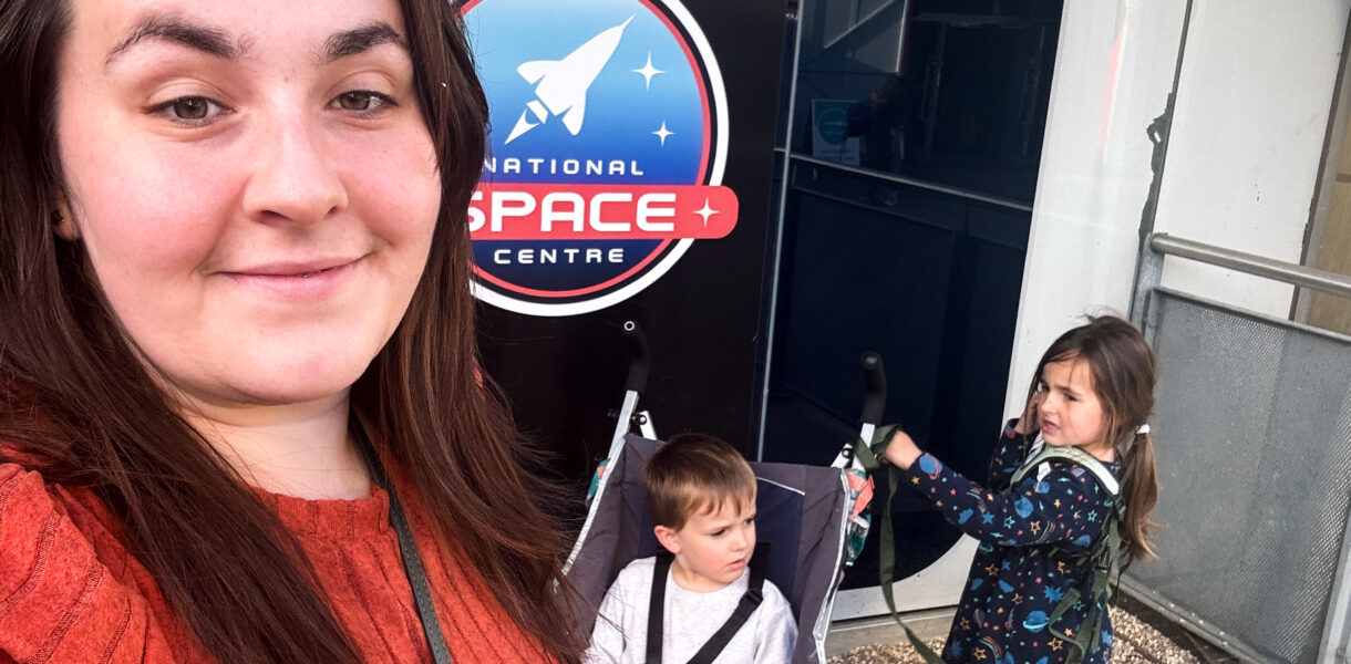 Alex stands in front of a National Space Centre sign with her two young twins