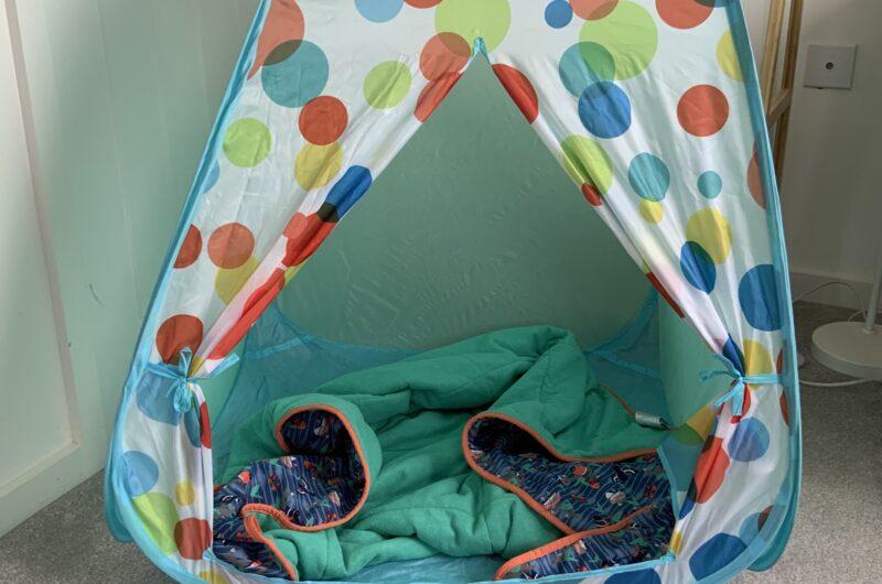 a pop up play tent with a spotty design and a blanket inside